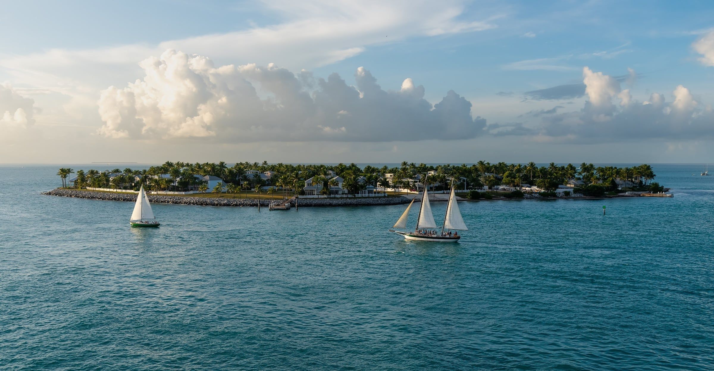 Two sailboats passing Sunset Key off Key West, palm trees and cumulus clouds over turquoise water